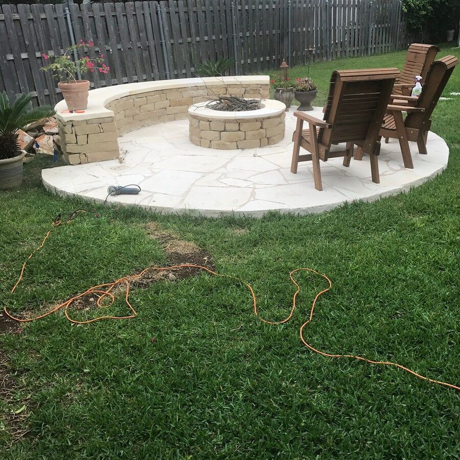 A backyard with a fire pit and chairs in the grass
