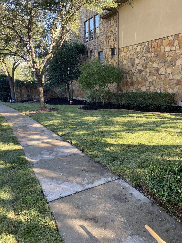 A sidewalk leading to a large stone building with a lush green lawn.