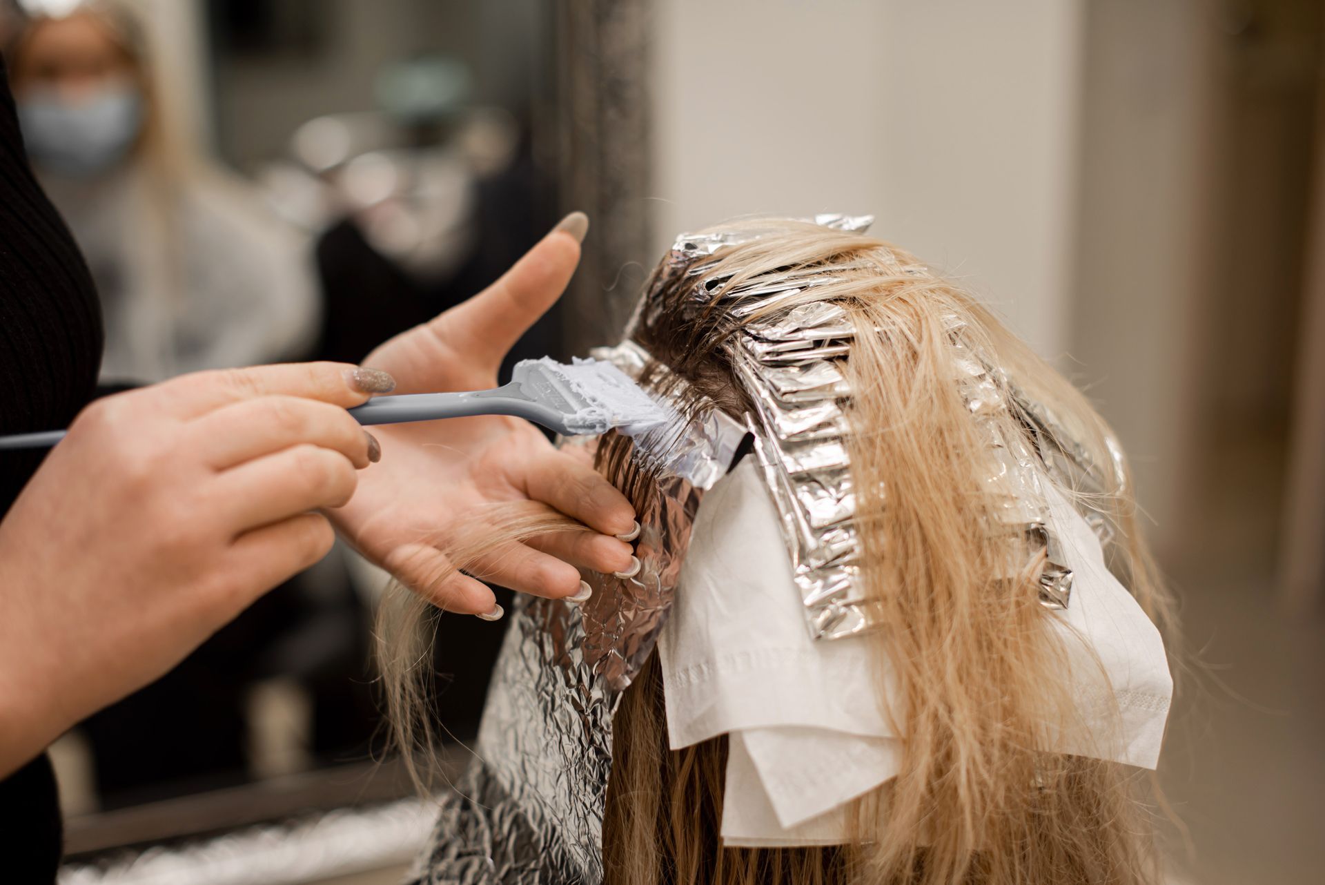 Hairdresser applying bleach to blonde hair with a brush and foil in a salon