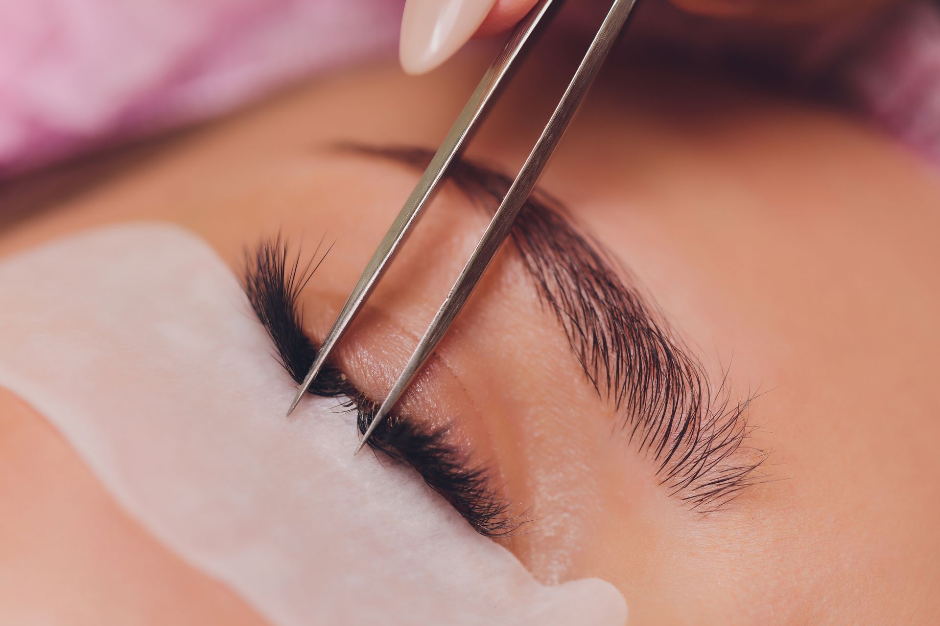 Close-up of eye with tweezers applying lash extensions