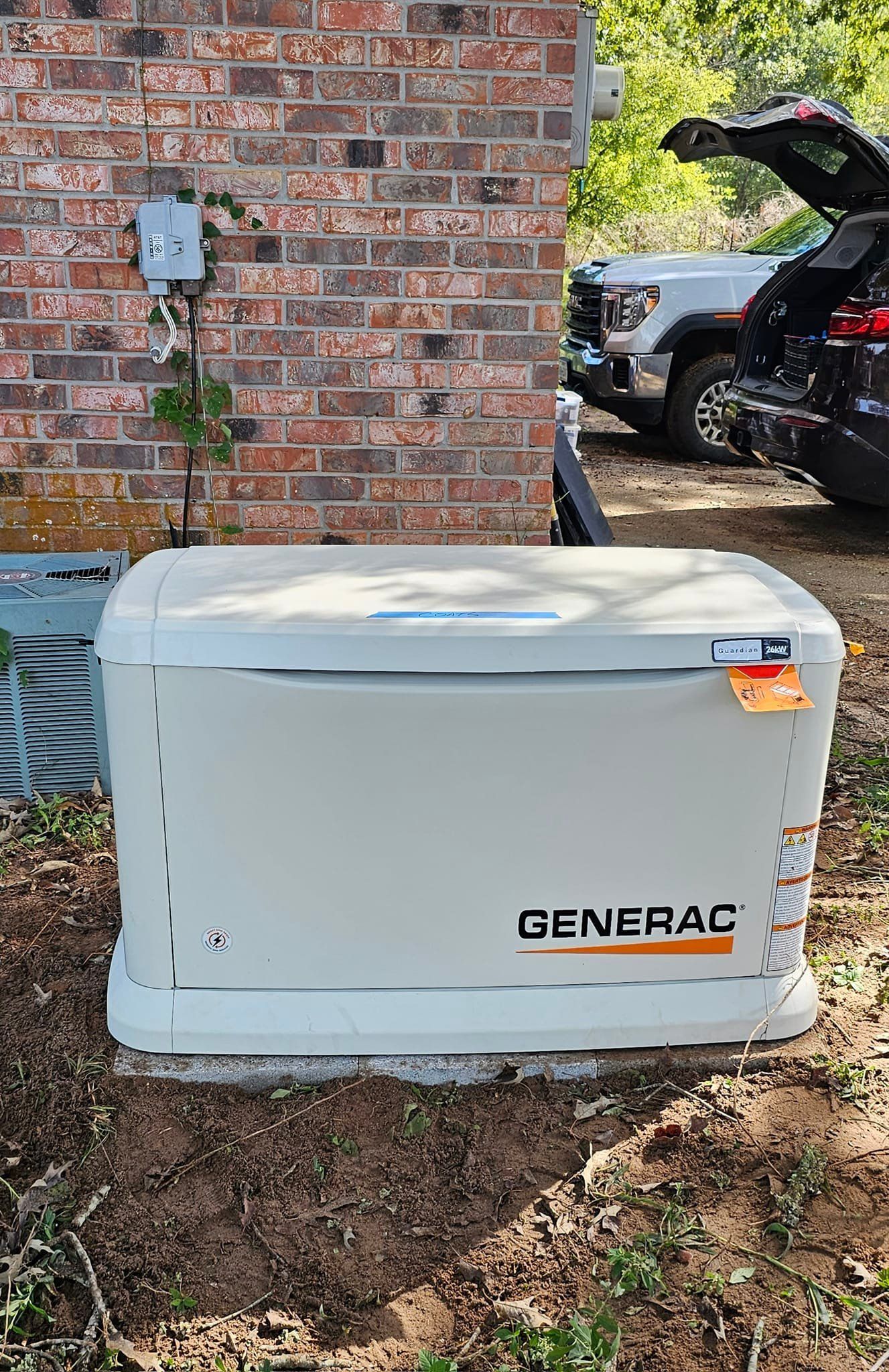 A generator is sitting in the dirt in front of a brick building.