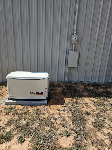 A generator is sitting in the grass in front of a building.