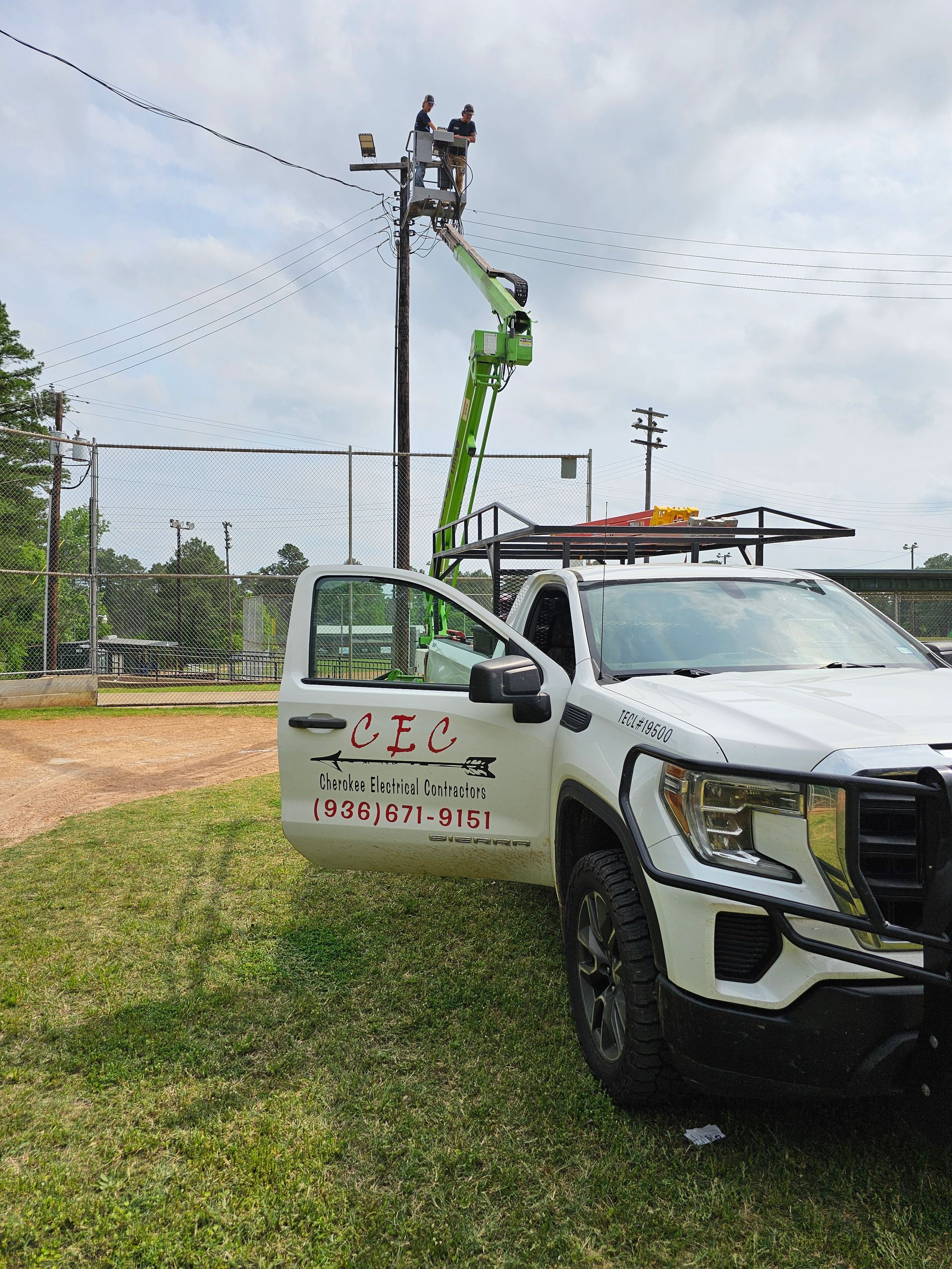 A white truck with a crane on top of it is parked in a grassy field.