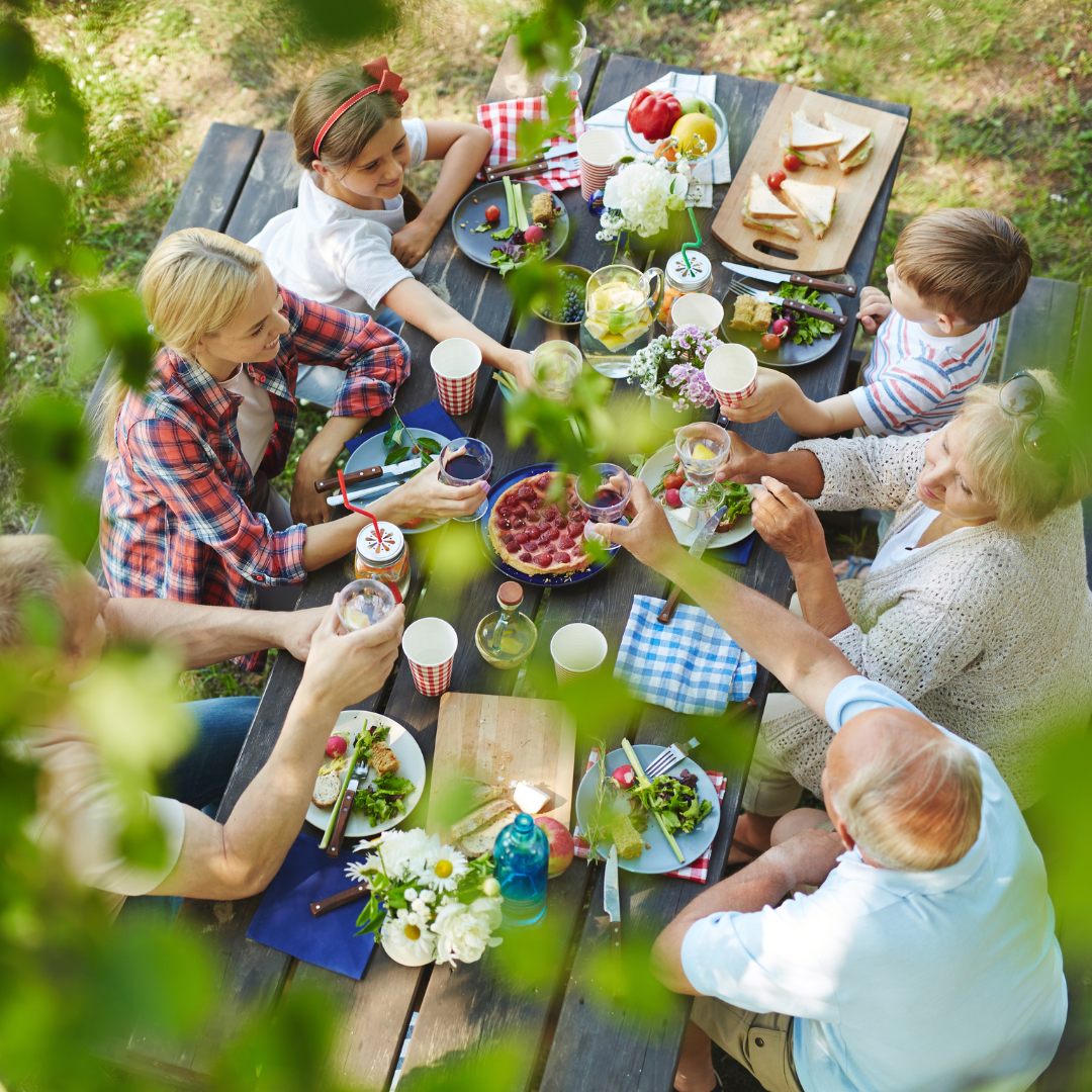 Family toasting together at a picnic table under trees.