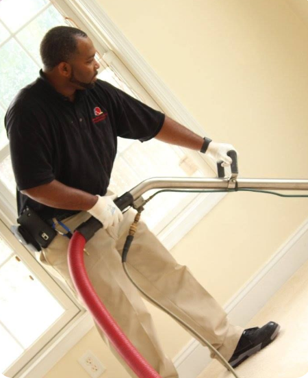 Worker vacuuming carpeted stairs with a backpack vacuum and long hose