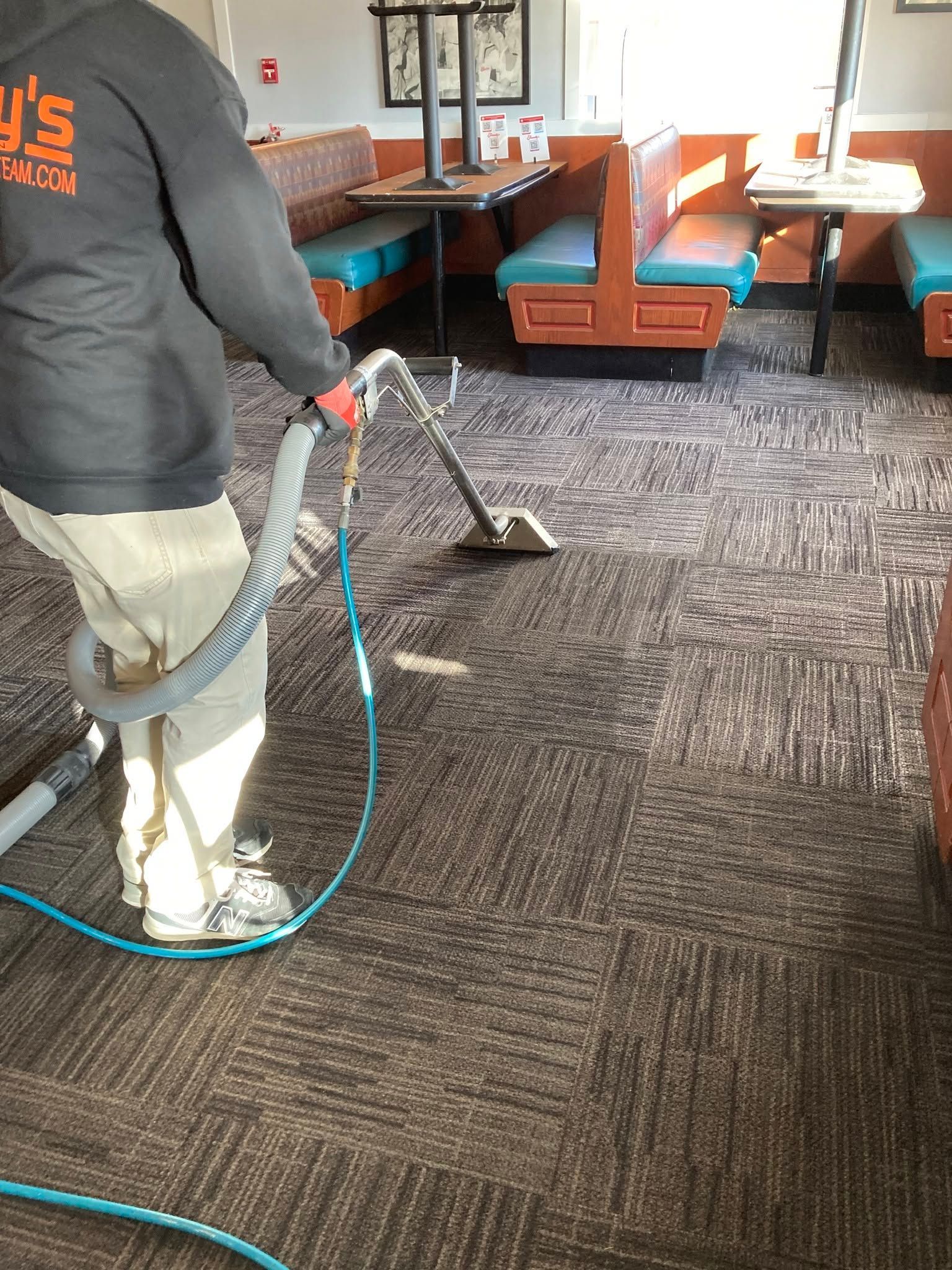 Person cleaning a carpet in a restaurant booth area with a wet vacuum hose.