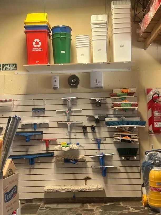 Pared de almacenamiento organizada con herramientas de limpieza, contenedores de reciclaje y suministros en estantes.