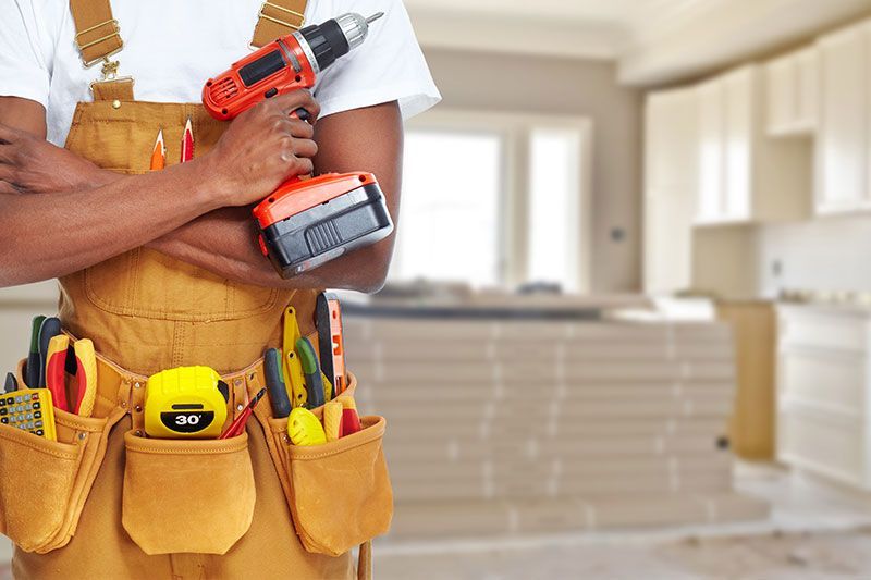 Carpenter holding a drill, wearing a tool belt, in a room under construction.