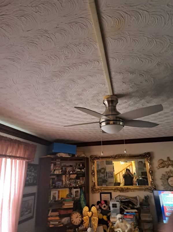 Ceiling fan in a room with textured ceiling, furniture, and a framed mirror.