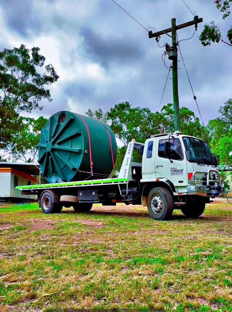White utility truck carrying a large green cable spool in a grassy field under cloudy skies — Full Torque Transport In Parkhurst, QLD