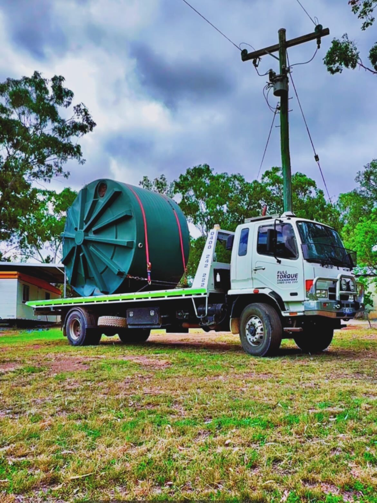 White flatbed truck carrying a large green industrial spool on a grassy roadside under cloudy sky — Full Torque Transport In Parkhurst, QLD 