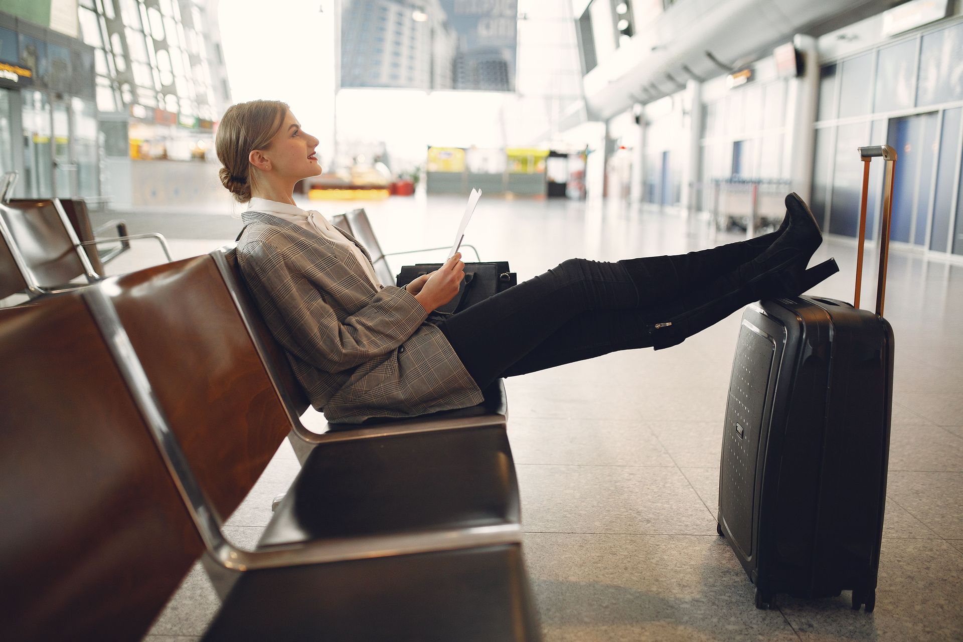 Traveler sitting on an airport bench with feet on a suitcase, waiting in a terminal