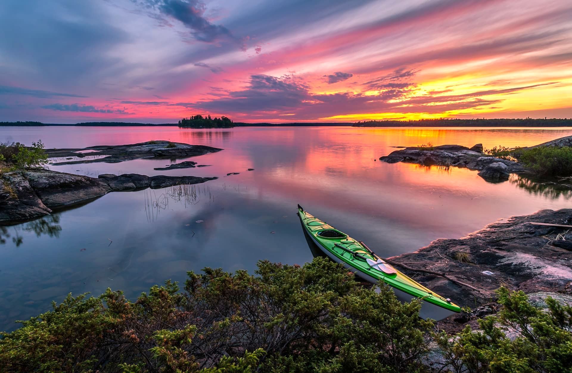 A green kayak is sitting on the shore of lake ontario at sunset.