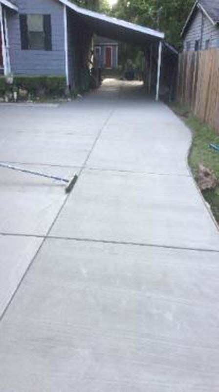 A concrete driveway leading to a house with a carport.