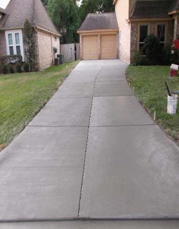 A concrete driveway leading to a house with two garage doors.