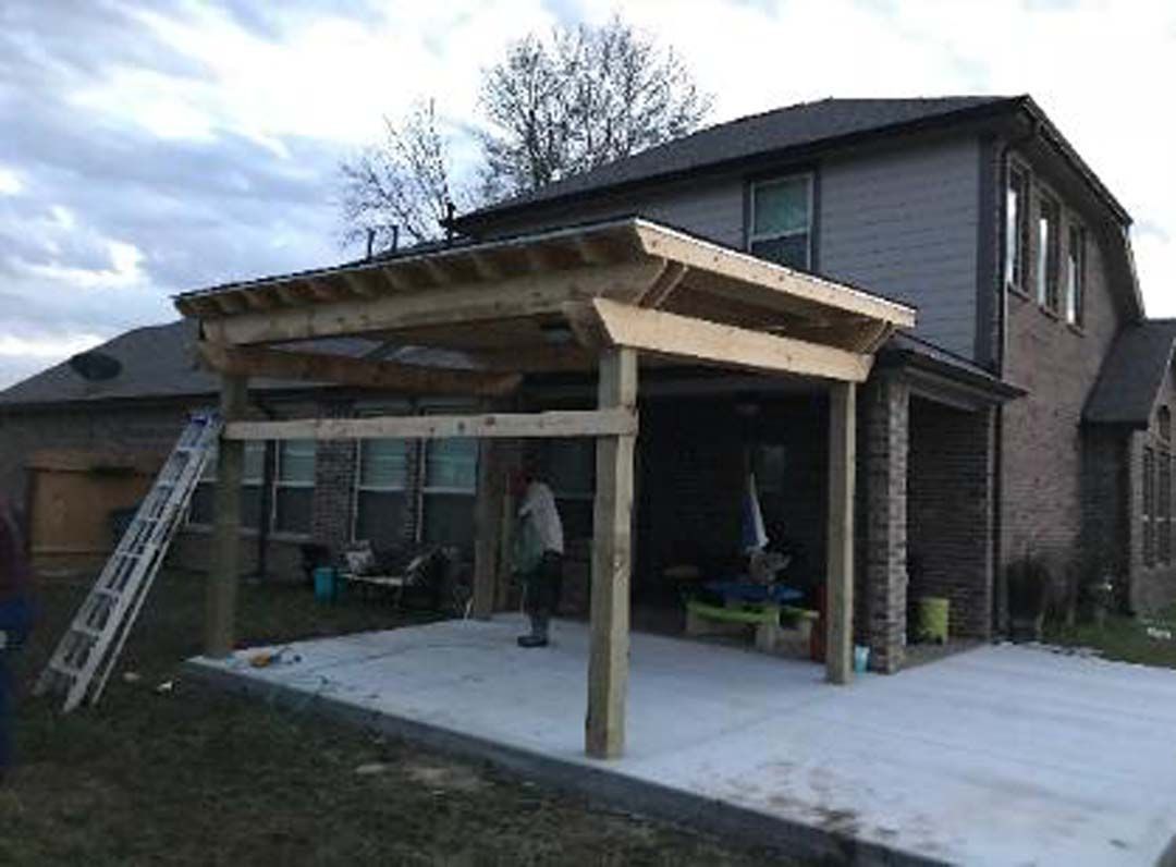 A man is standing under a wooden pergola in front of a house.