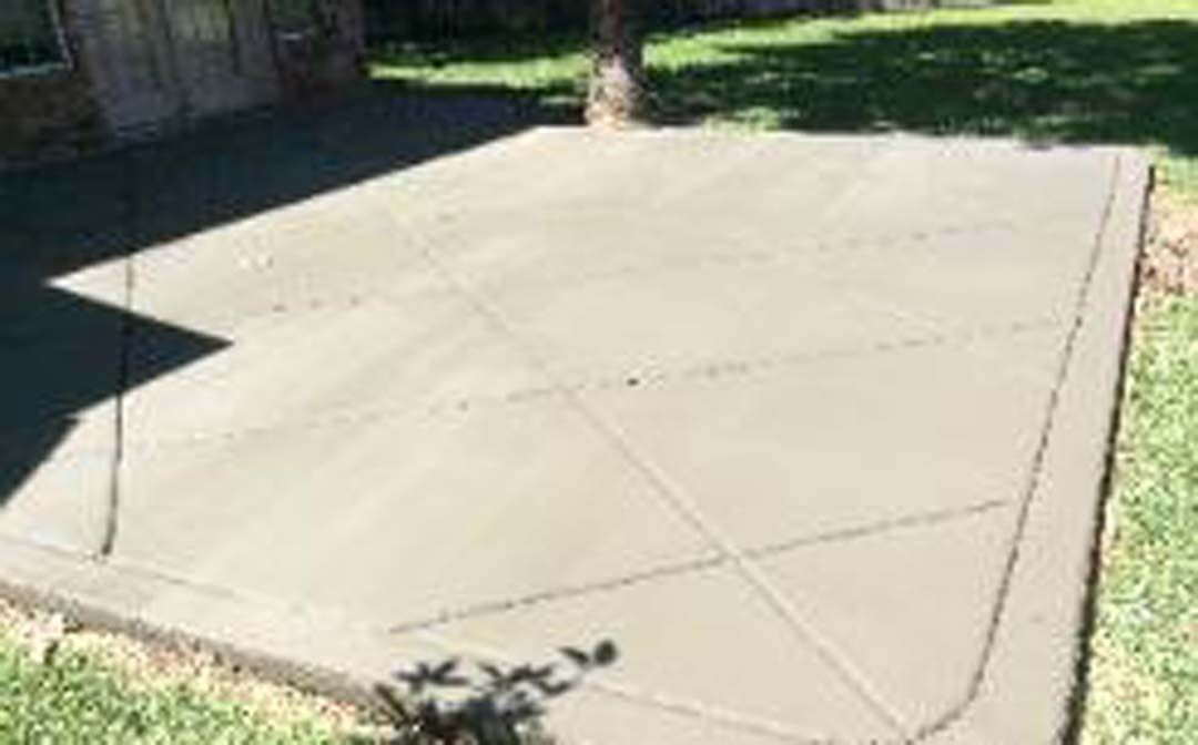 A concrete patio is being built in the backyard of a house.