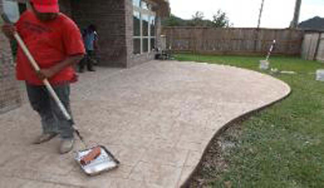 A man is painting a concrete patio with a roller.