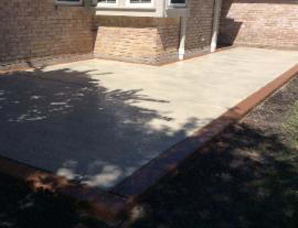 A concrete patio in front of a house with a brick border.