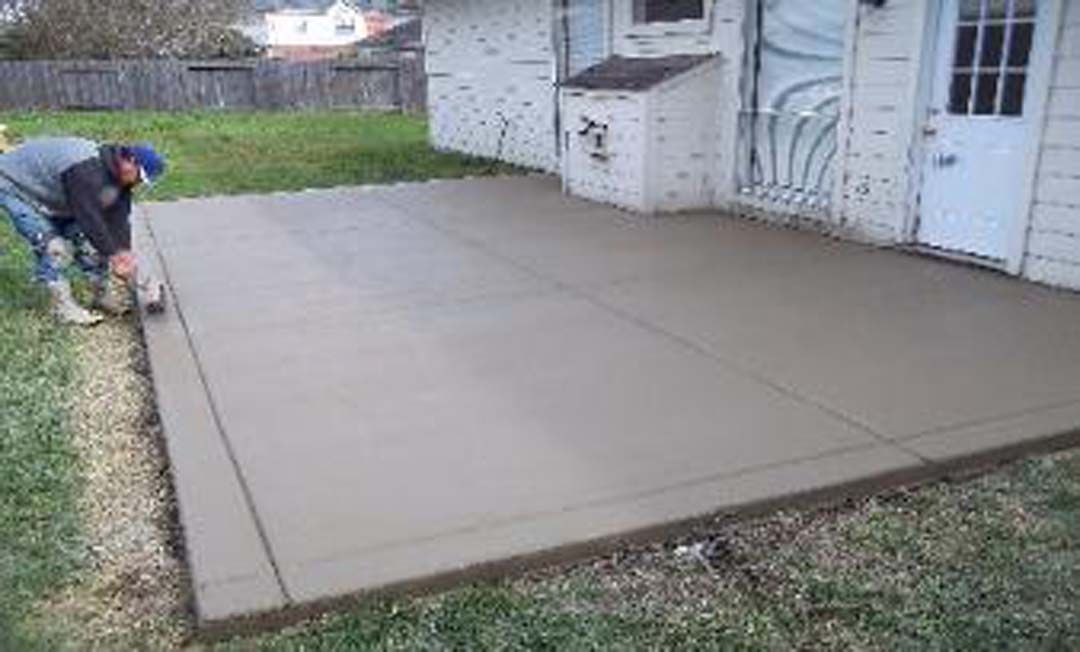 A man is laying concrete on a patio in front of a house.