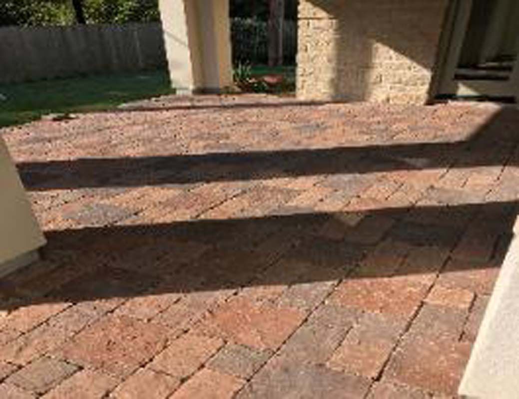 A brick patio in front of a house with a fence in the background.