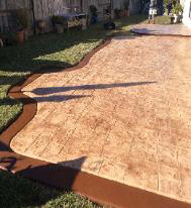 A concrete patio with a brown border is sitting on top of a lush green lawn.