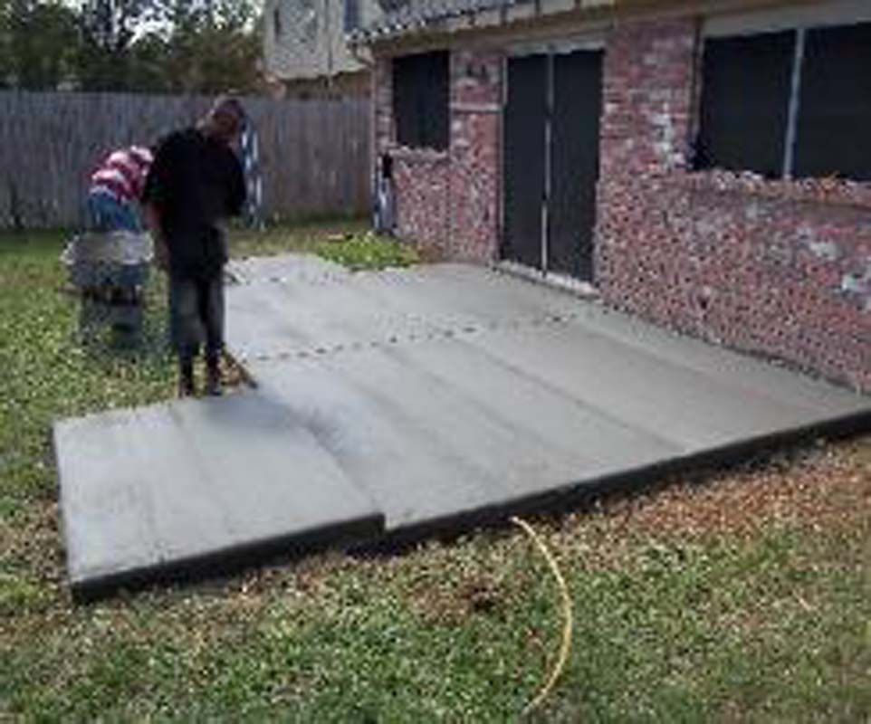 A man is standing on a concrete patio in front of a brick house.