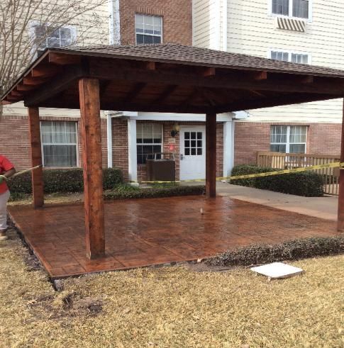 A man is standing under a wooden gazebo in front of a building