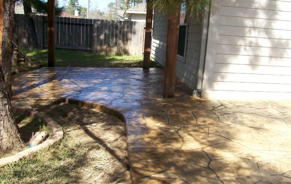 A concrete walkway leading to a house with a fence in the background.