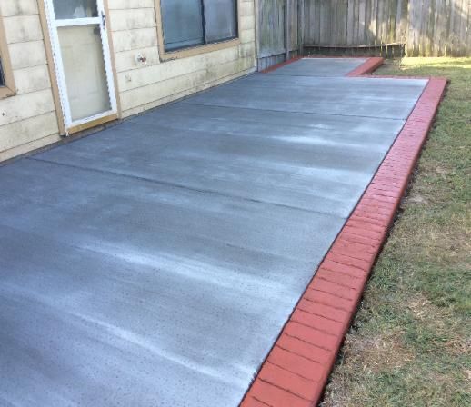 A concrete patio with a red brick border is in front of a house.