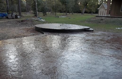 A concrete circle in the middle of a muddy field with a house in the background.