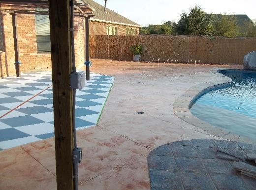 A patio with a checkered pattern and a pool in the background