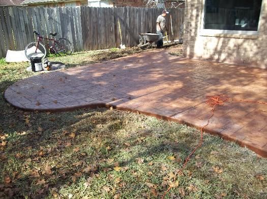 A man is working on a patio in the backyard of a house.