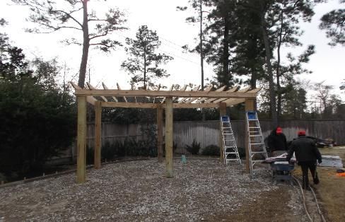 A group of people are working on a wooden pergola in a backyard.