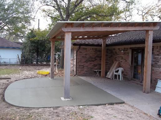 A wooden pergola is sitting on top of a concrete patio in front of a brick house.