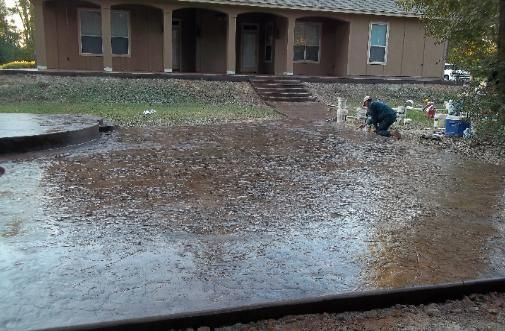 A man is working on a concrete driveway in front of a house