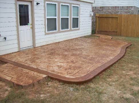 A concrete patio in front of a house with a wooden fence in the background.