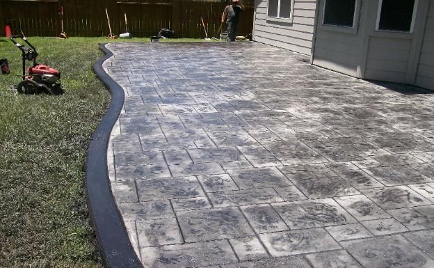 A concrete driveway is being built in a backyard next to a house.