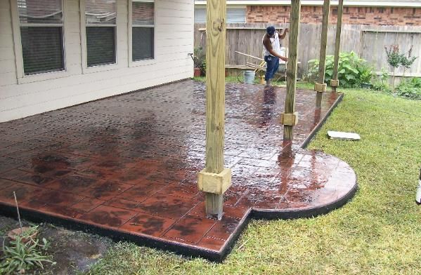 A man is painting a concrete patio in front of a house.