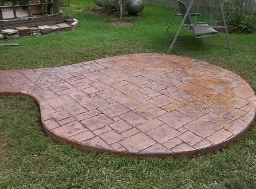 A circular concrete patio in a backyard with a swing in the background.