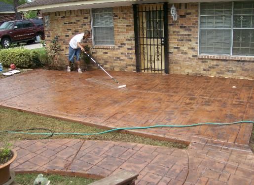 A man is cleaning a concrete patio in front of a brick house.