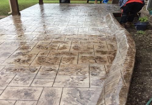 A man is working on a concrete patio with a hose.
