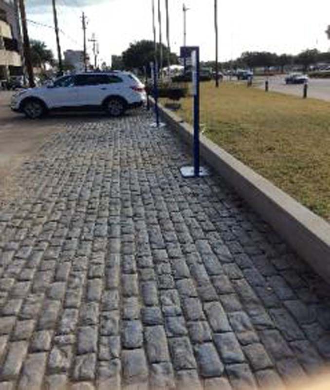A white suv is parked on a cobblestone sidewalk.