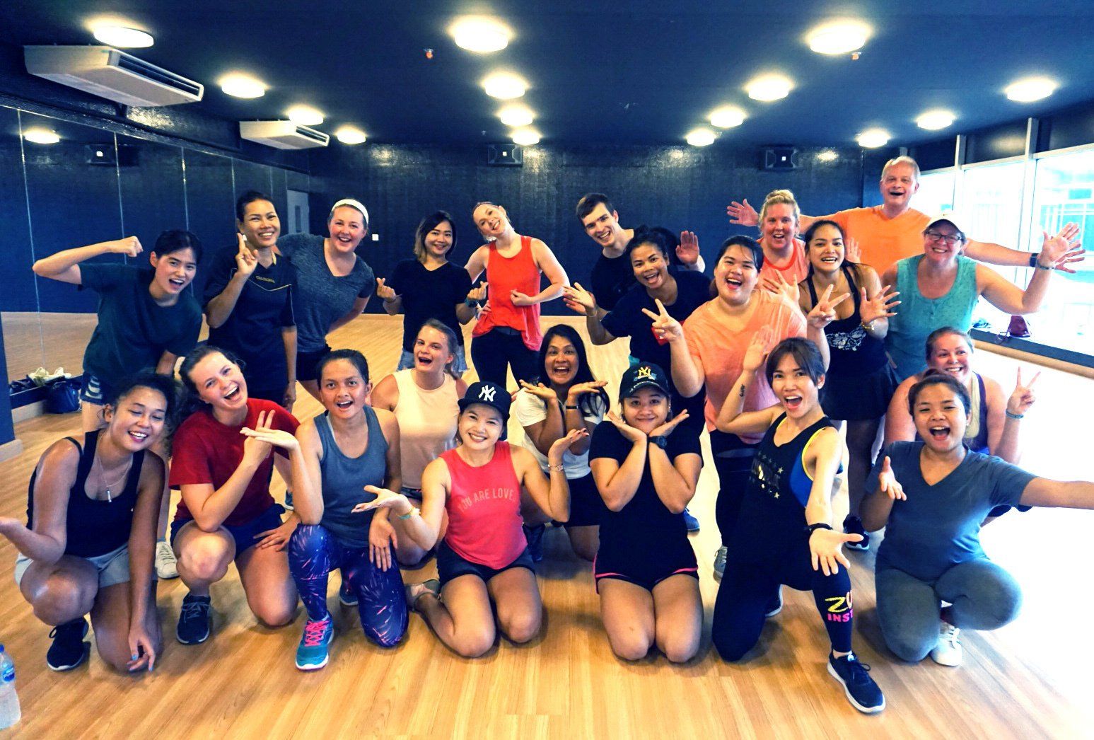 Group of people posing together in a dance studio, smiling and making hand gestures.