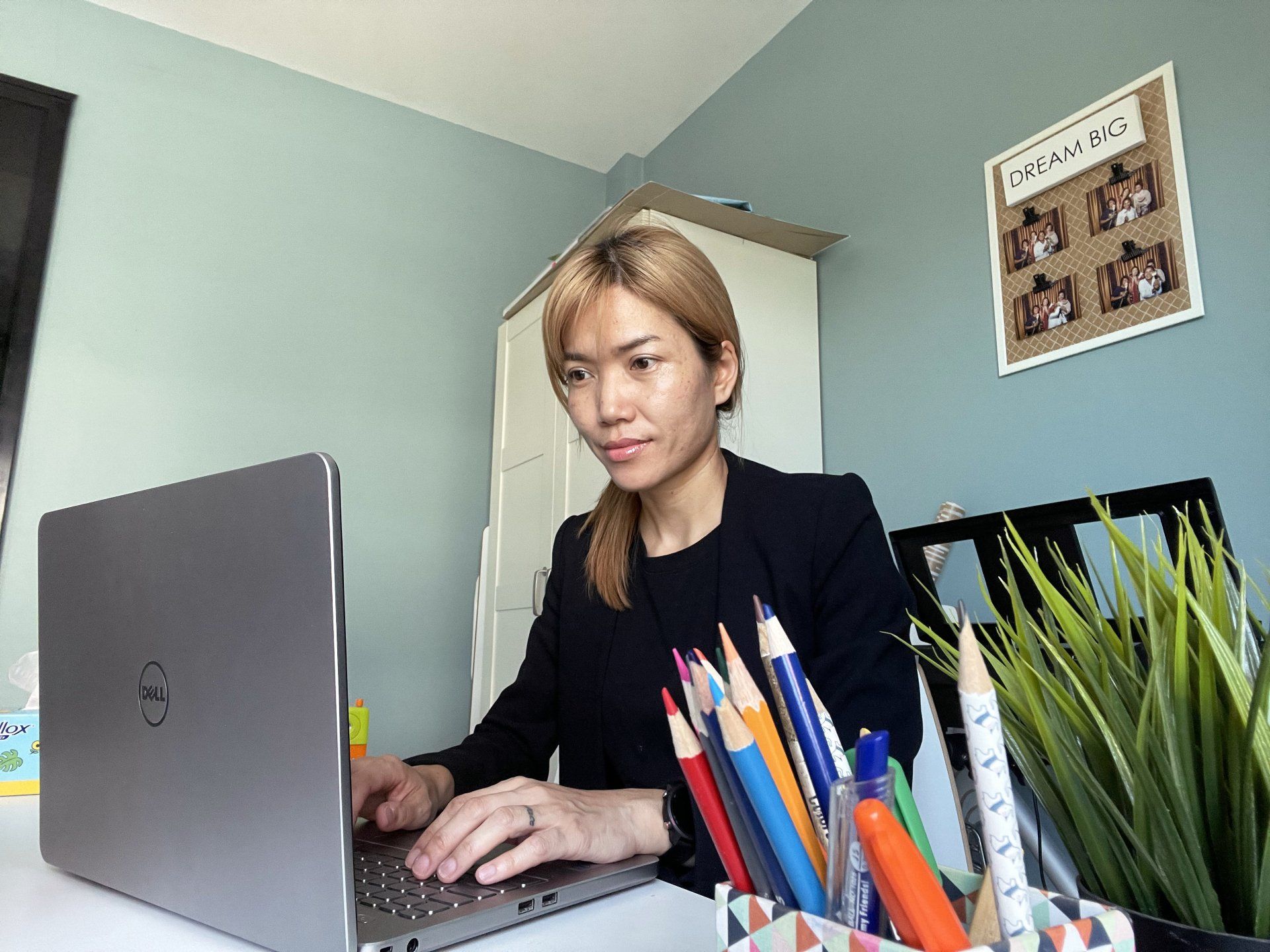 Woman in black blazer working on a laptop at a desk with colored pencils.