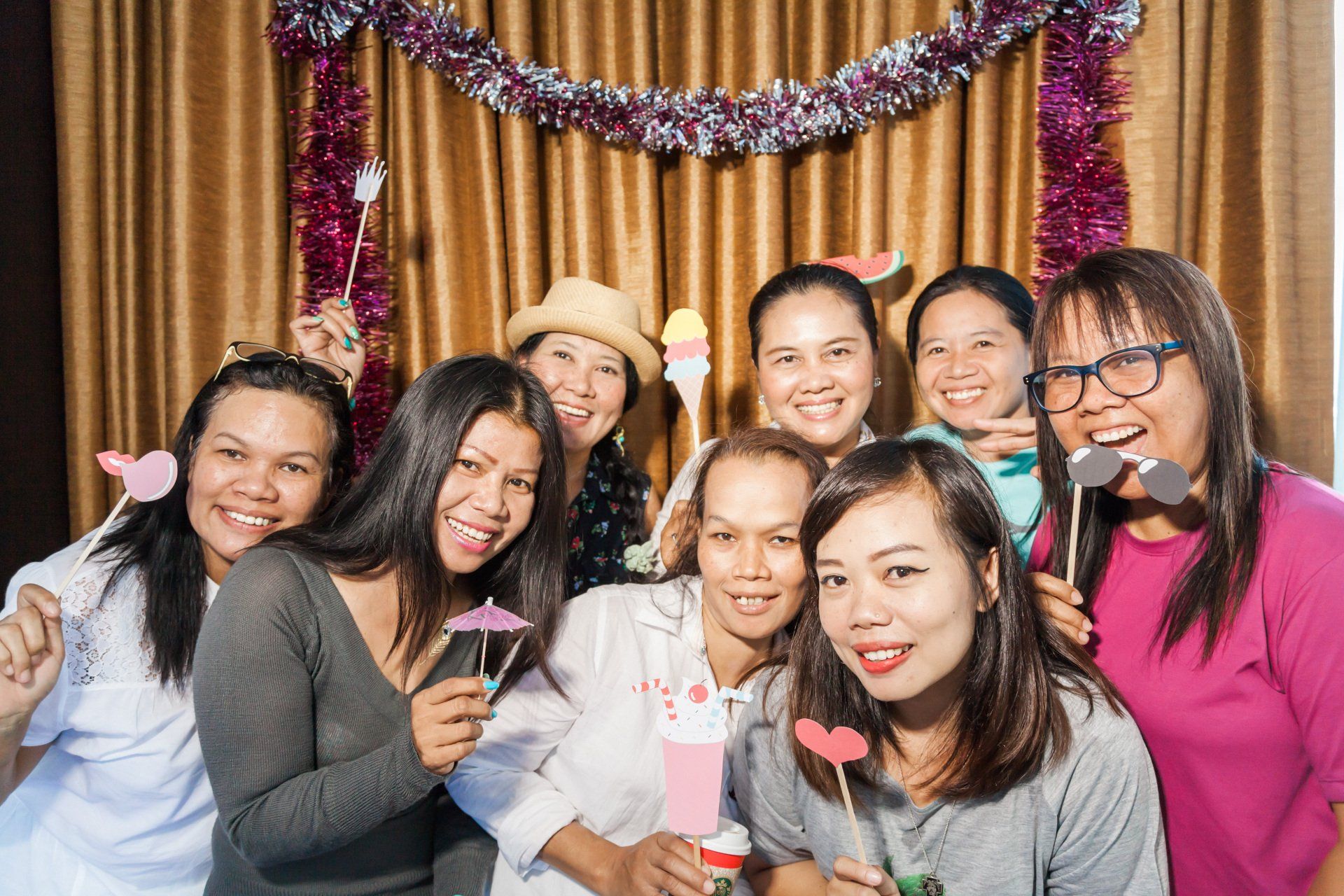 Group of smiling people with photo props in front of a curtain decorated with tinsel.