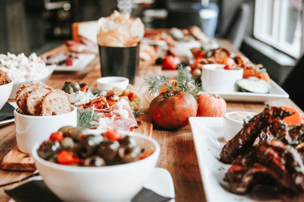 Wooden table laden with assorted food: charcuterie, vegetables, bread, and dips.