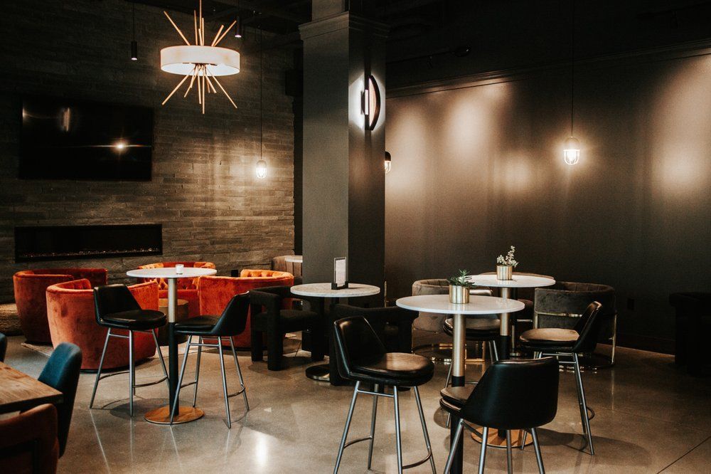 Stylish, dim-lit lounge area with tables, chairs, and velvet seating. Dark walls, concrete floor, modern lighting.