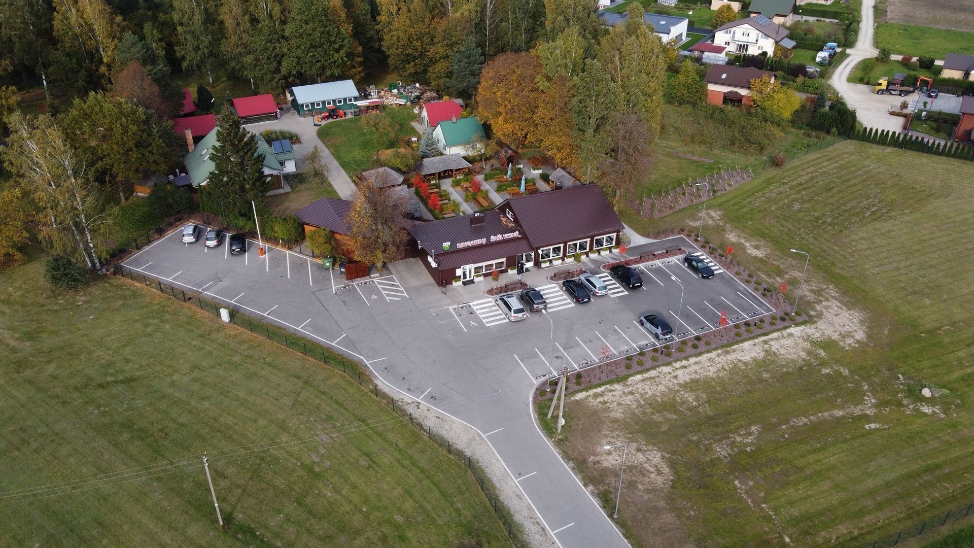 Užeigos su automobilių stovėjimo aikštele, apsuptos medžių ir laukų, vaizdas iš oro