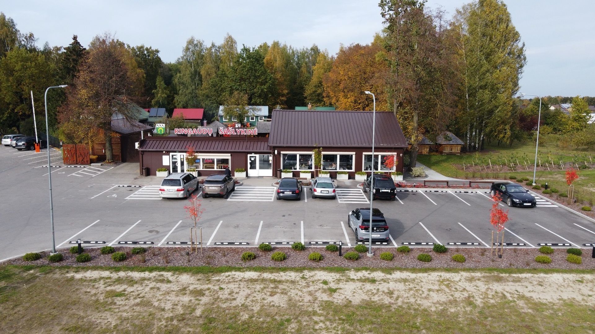 Restoranas su automobilių stovėjimo aikštele, apsupta rudeninių medžių.
